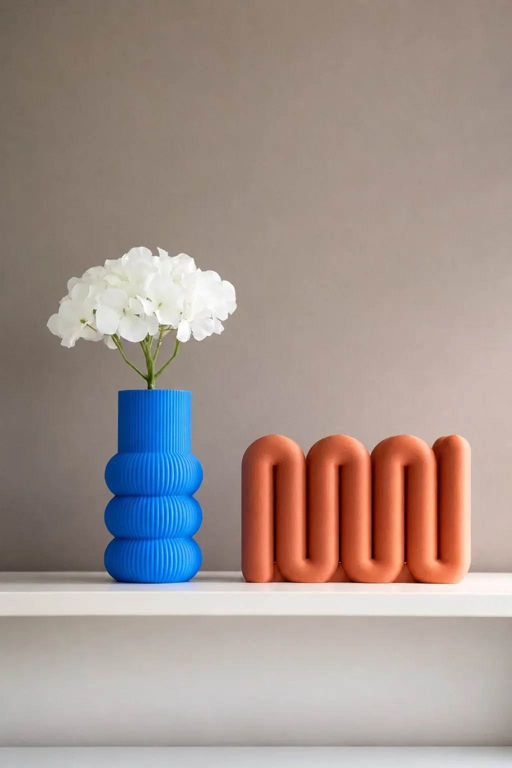 Florero azul y escultura naranja impresos en 3D sobre una superficie clara