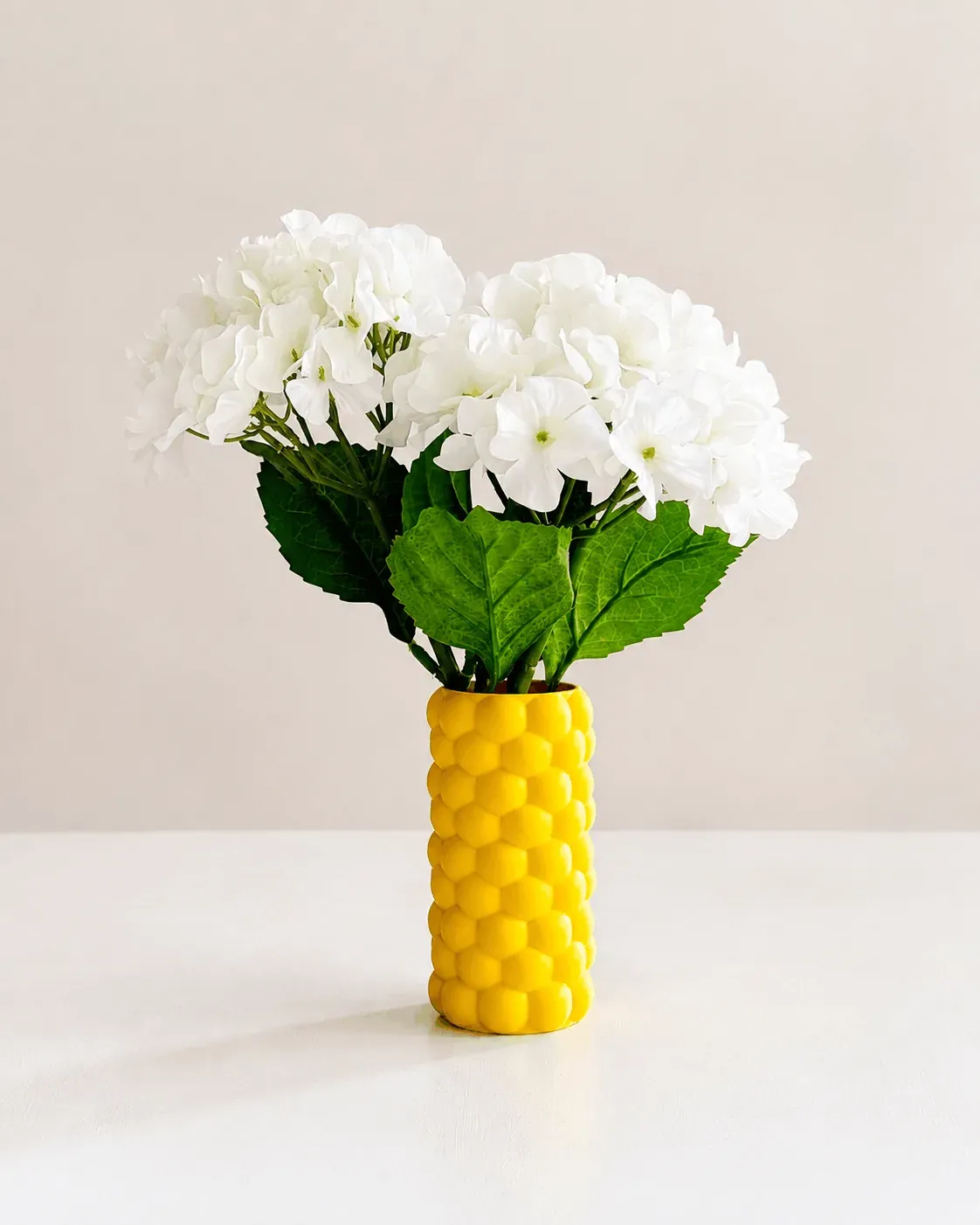 Florero Colmena amarillo con un ramo de hortensias blancas sobre una mesa clara