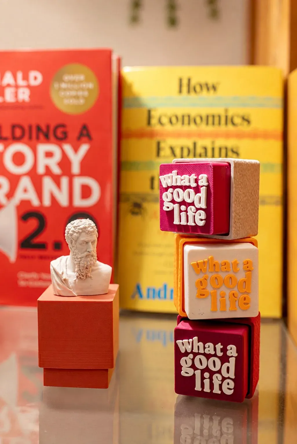 Clicker Aristóteles junto a cubos impresos que dicen «what a good life», frente a una repisa de libros