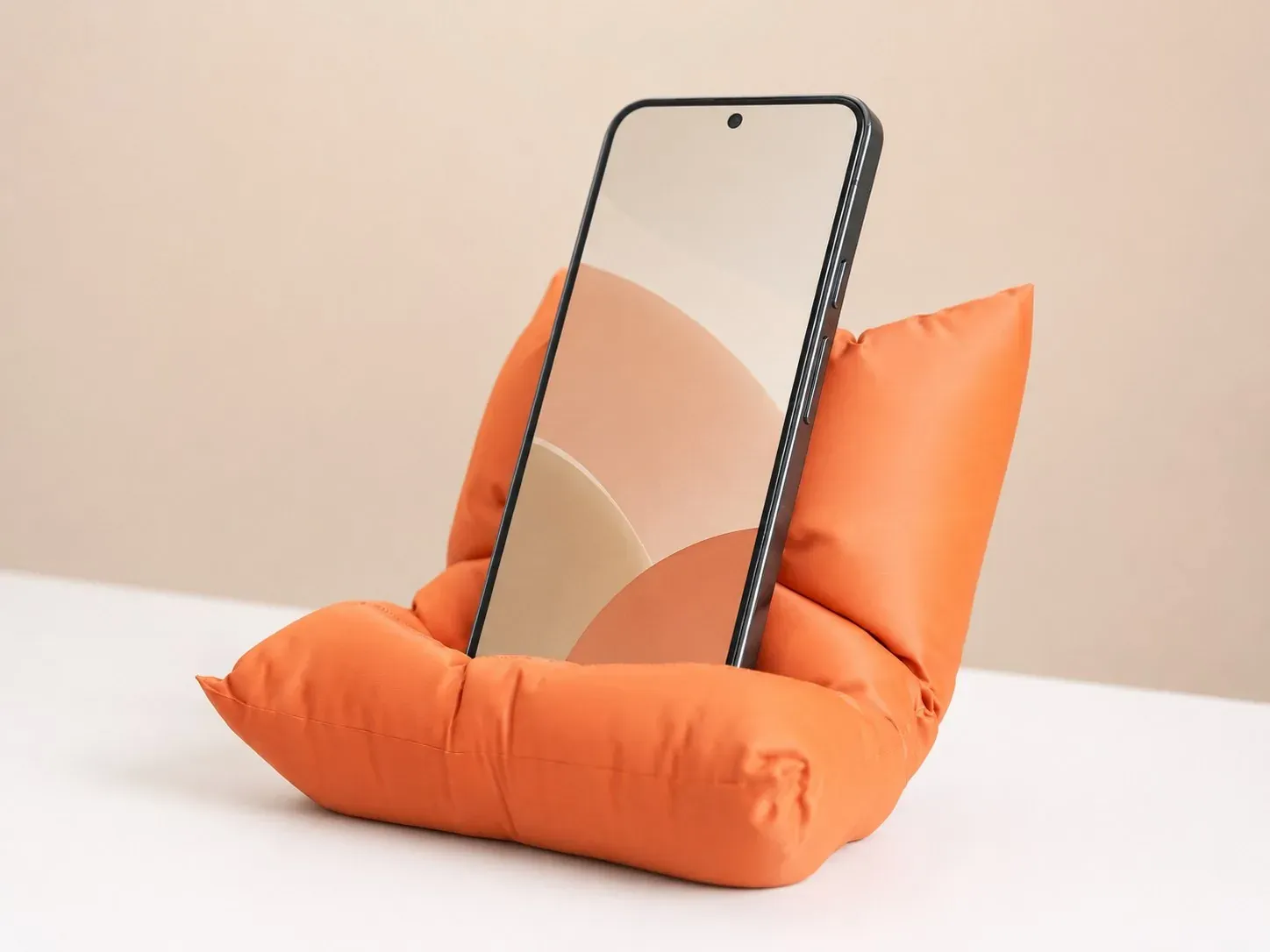 Celular apoyado en el cojín soporte naranja, en ángulo sobre una mesa blanca