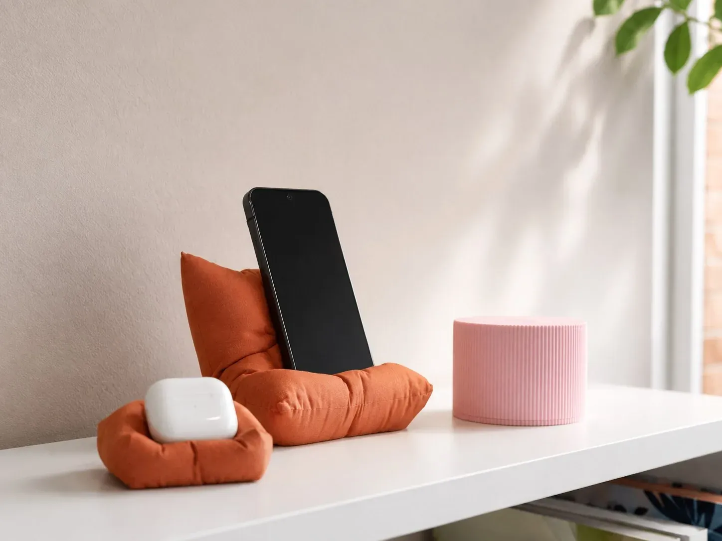 Escritorio con el cojín soporte naranja sosteniendo un celular, el soporte pequeño con audífonos y la alcancía rosada