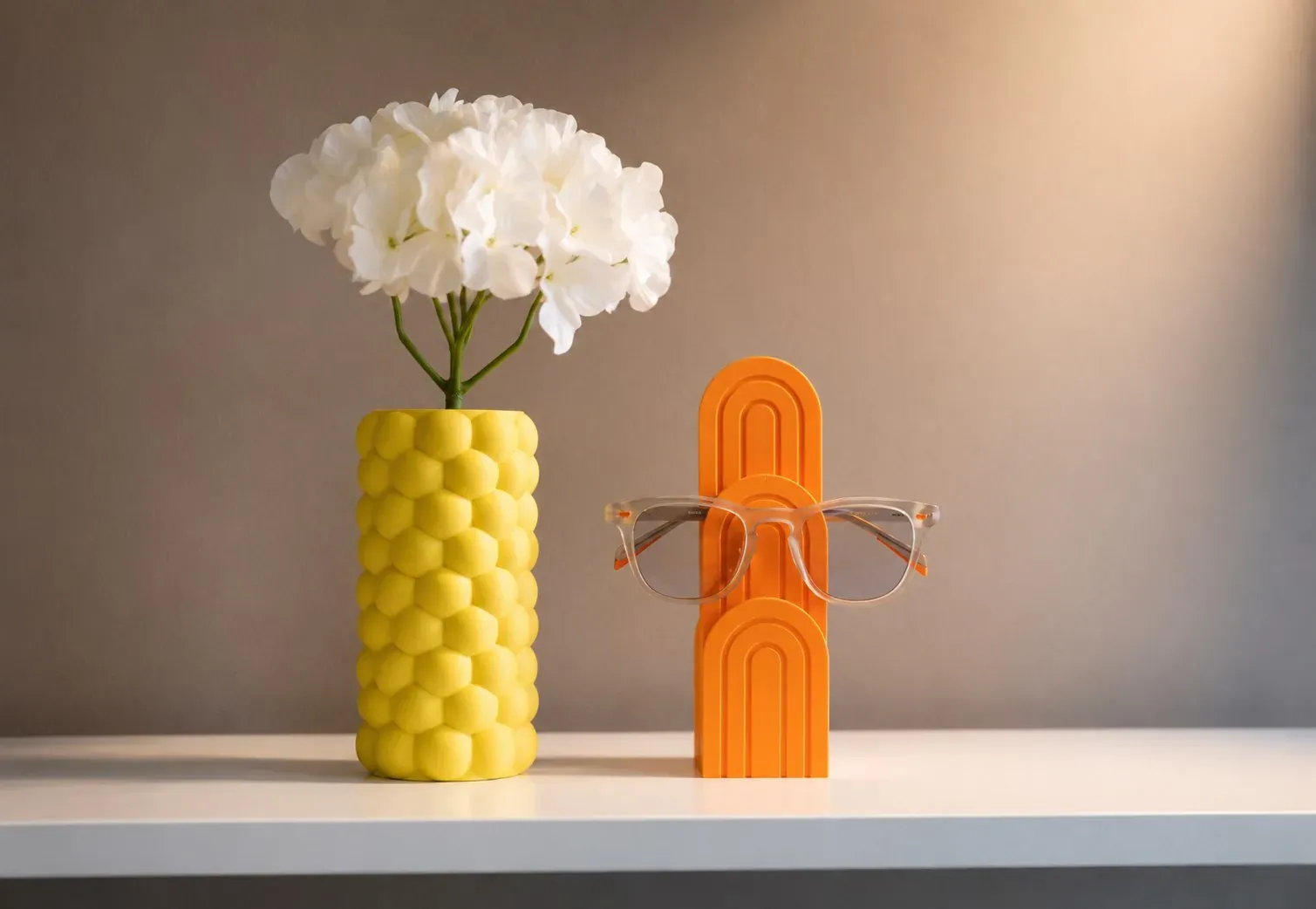 Florero Colmena amarillo con flores blancas junto al Arco para Gafas naranja en una repisa